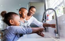 Mother and children washing hands at kitchen sink